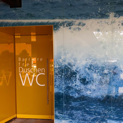 Eingang zu den barrierefreien Duschen des Freibads. Die Türe ist Orange.