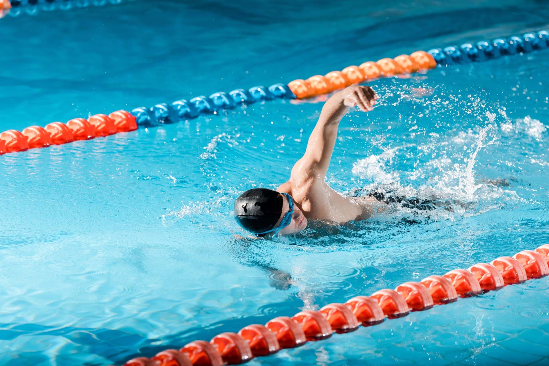 Mann mit schwarzer Badehaube und blauer Taucherbrille schwimmt im 50 Meter Sportbecken des Freibads Mammendorf.