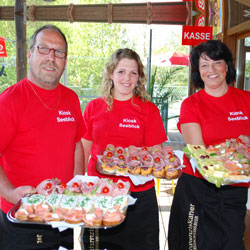 Kiosk Mitarbeiter mit roten T-Shirts präsentieren kalte Platten mit belegten Brötchen und lachen in die Kamera