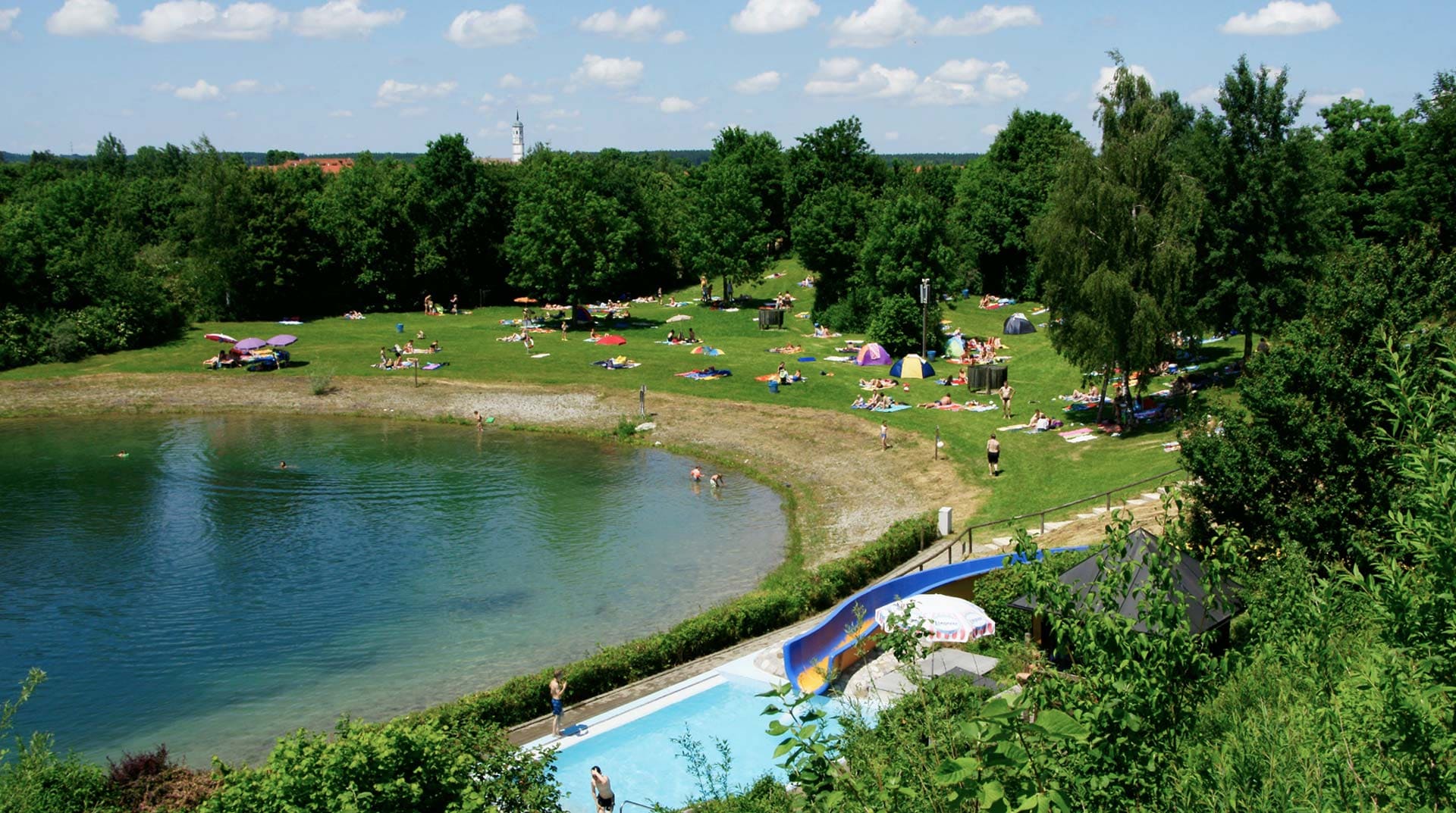 Gut besuchte Liegefläche des Freibadsees bei schönem Wetter