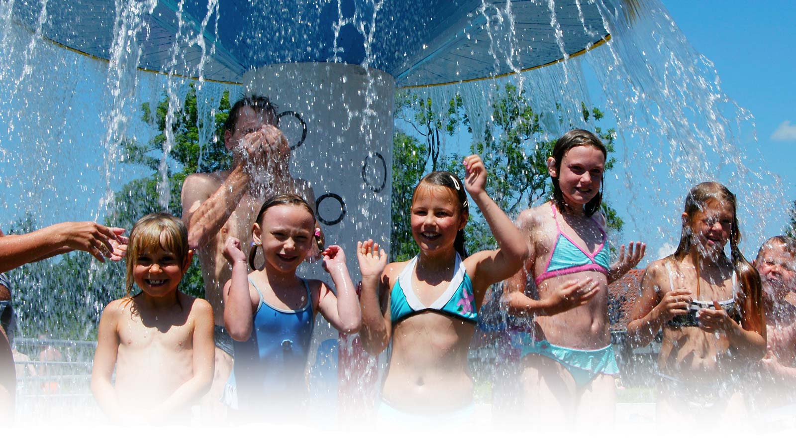 Lachende junge Mädchen stehen unter dem plätschernden Wasserpilz des Freibad Mammendorf