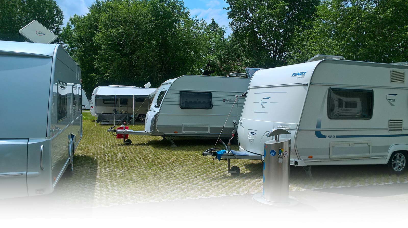 Vier weiße Wohnmobile stehen auf dem Parkplatz des Zeltplatzes Mammendorf